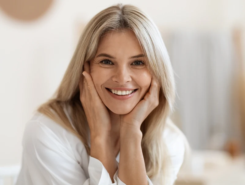 50s woman with smooths skin smiling at the camera